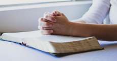 hands praying over an open Bible
