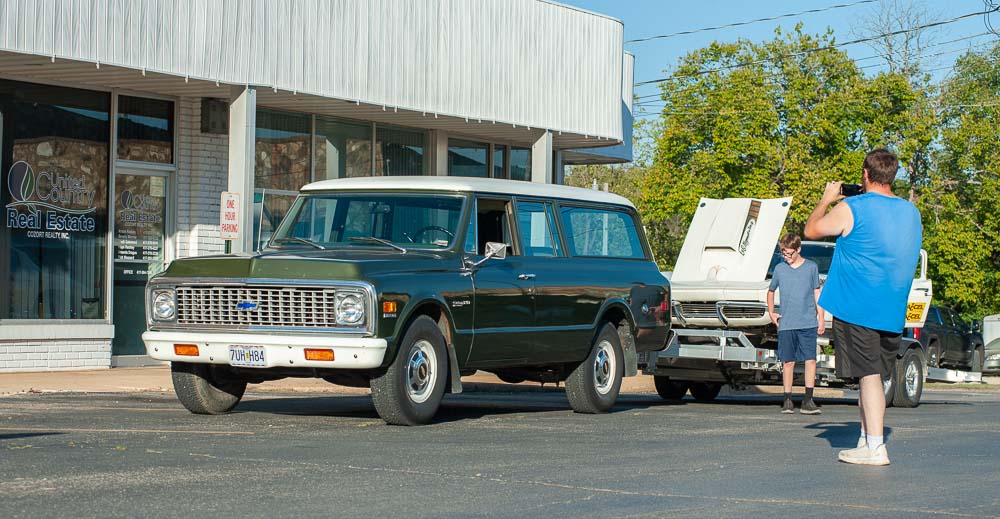 A classic dark green car being admired on the square at the cruise-in.
