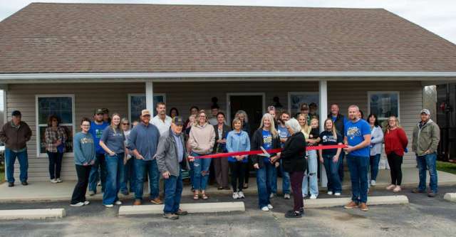 Individuals and representatives for various businesses pose for the ribbon cutting at United Country.